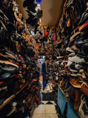 A narrow aisle in a vintage shoe store filled with various shoes and a person browsing.