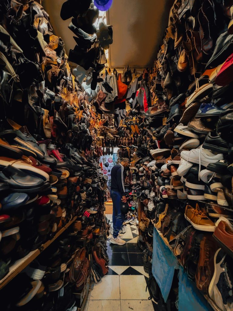 A narrow aisle in a vintage shoe store filled with various shoes and a person browsing.